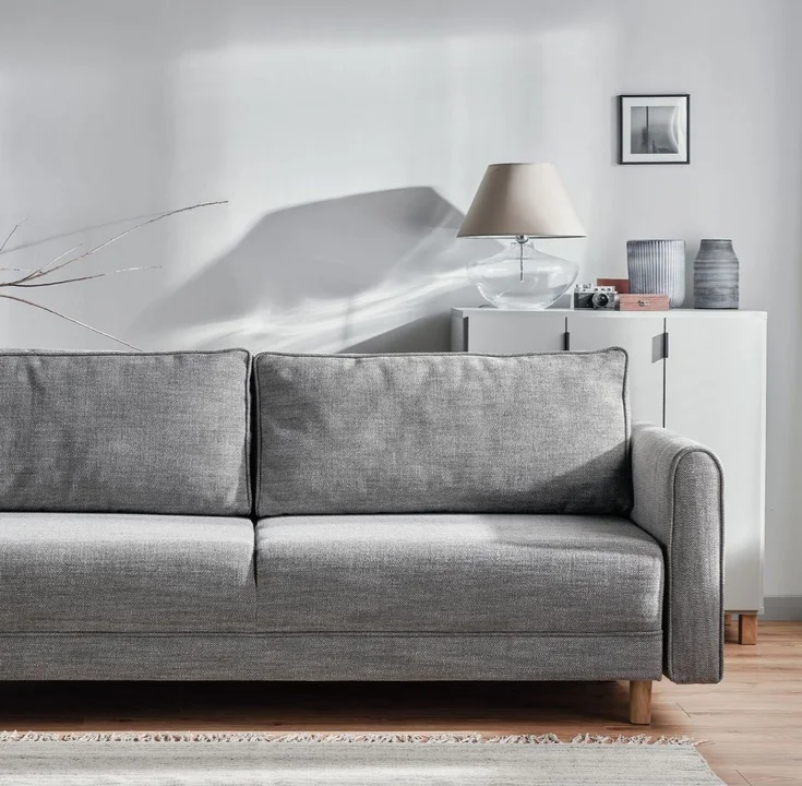 Szara sofa w jasnym salonie z delikatnymi dekoracjami.